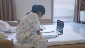 Sick asian child learning online class with teacher and friend at hospital. Sick kid writing a book while studying online class video call zoom in classroom while stay in hospital. Slow motion shot.