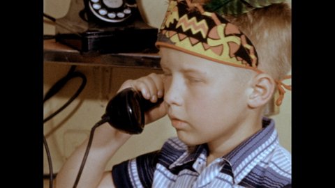 1950s: Slate. Boy in headdress talks on a telephone receiver then hangs up. Slate. Hands unwrap a telegraph set. They open the box to reveal wire, batteries and telegraph keys.