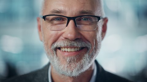 Portrait of Successful Middle Aged Bearded Man Looking at Camera and Smiling. Handsome Senior Businessman Wearing Jacket Rising Eyes, Having Fun. Close-up Shot