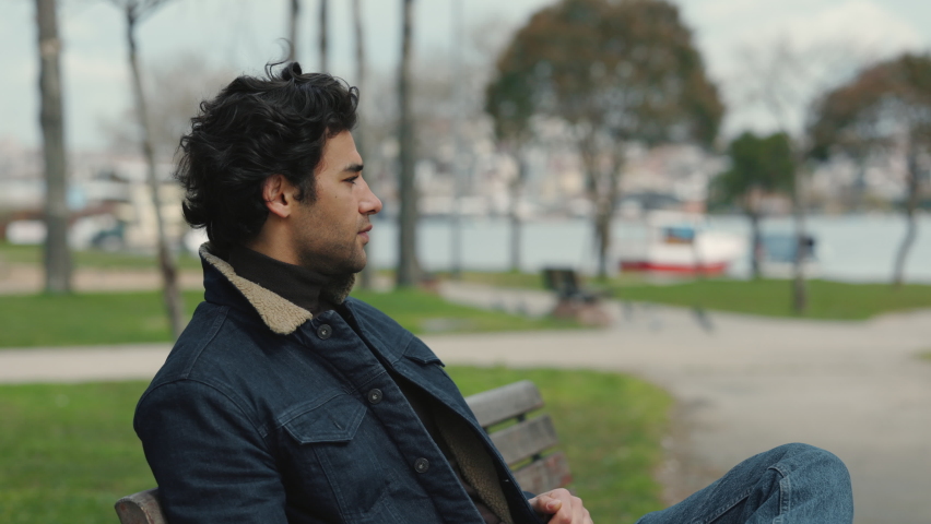 Confident arabian man in stylish clothes sitting on bench at city park an looking at camera. Handsome guy with dark hair enjoying free time on fresh air. Royalty-Free Stock Footage #1081614677