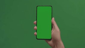 Hand Holding Cell Phone With Green Screen In Green Background
