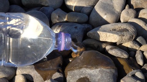 Water flows out of an overturned bottle onto stones, "gulping" effect. 