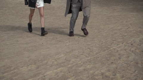Young couple runs along the sandy beach. Man and woman on wedding day or honeymoon vacation. Bride and groom enjoy summer, romantic date. Male in gray suit, woman in short white dress and black shoes.
