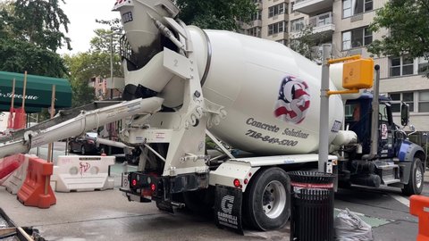 NYC, USA - OCT 12, 2021: concrete mixer spinning chute feeder pouring cement onto pavement workers smoothing New York City audio.