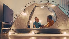 Father and son watching smartphone, talking on video call phone in tent with Christmas decorations in home. Family online chat. Long distance communication. Staying connected.