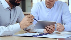Two diverse business men discussing analyzing financial market data using digital tablet. Financial advisor broker manager consulting investor client managing project tech at office meeting. Closeup - Powered by Shutterstock - Get 15% off with code: PIKWIZARD15