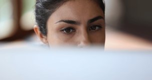 Close up face of focused young Indian female looking on computer screen reading document online thinking on information doing remote job. Concentrated millennial woman practice distant work learning