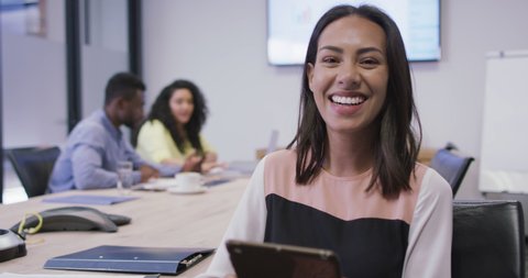 Portrait of smiling biracial businesswoman using tablet looking at camera in modern office. business and office workplace.