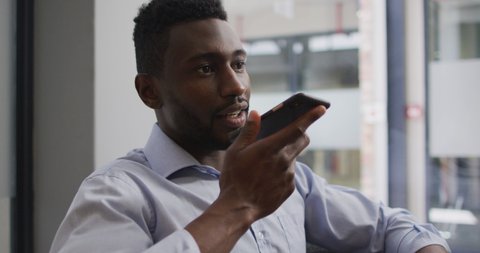 Worried african american businessman sitting in armchair talking on smartphone in modern office. business and office workplace.