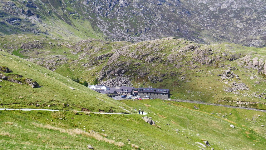 North Wales. High angle view of tourist or visitor building complex at Pen Y Pass in Snowdonia National Park mountains; distant people on Miners Track, cars driving past on A4086.