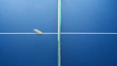 Overhead view of table tennis ping-pong ball bouncing over the net being hit from sides of blue table, motion blur effect.