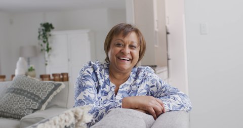 Portrait of happy african american senior woman on couch in living room, looking to camera smiling. retirement lifestyle, leisure time alone at home.