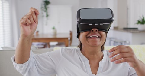 Happy african american senior woman sitting on couch enjoying using vr headset. retirement lifestyle, leisure time alone at home with technology. Video Stok
