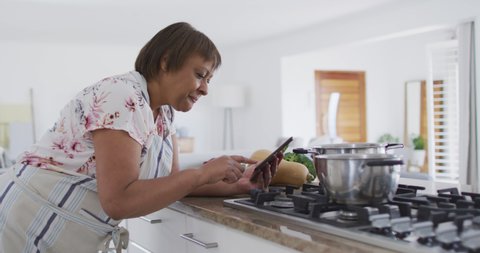 Happy african american senior woman preparing food in kitchen, using tablet and smiling. healthy, active retirement lifestyle with technology.
