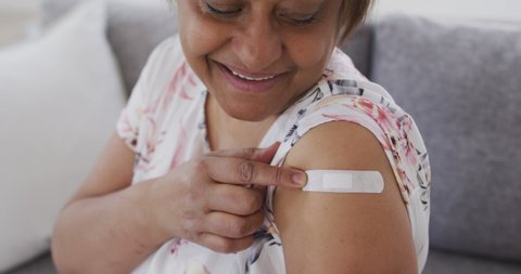 Smiling african american senior woman showing bandage on arm after covid vaccination. retirement healthcare and lifestyle during covid 19 pandemic.