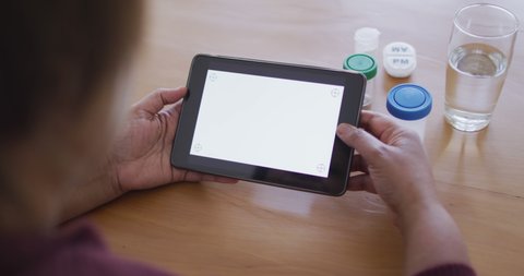 African american senior woman holding tablet with copy space on screen, medication bottles on table. retirement healthcare and lifestyle, at home with technology.