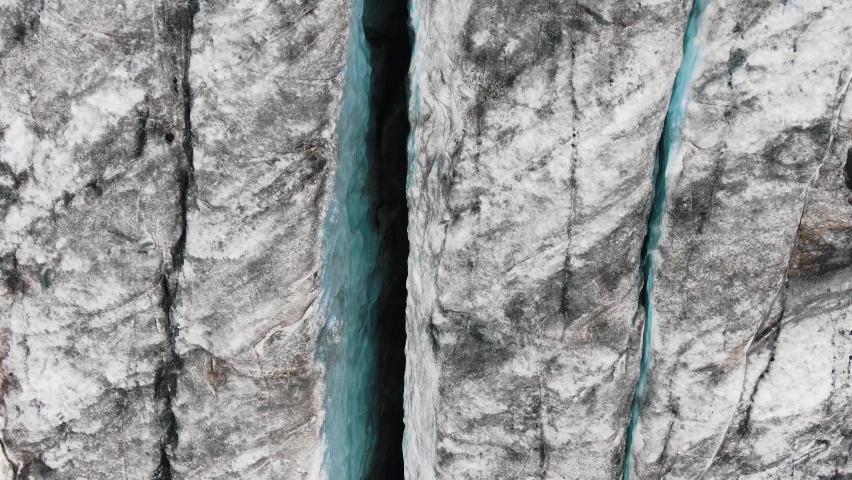 Large high grey cliffs with blue shadow rifts and big deep cracks covered with snow and black mineral products aerial view