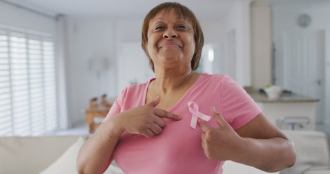 Portrait of smiling african american senior woman wearing pink t shirt and pink breast cancer ribbon. senior female lifestyle and breast cancer positive awareness campaign.