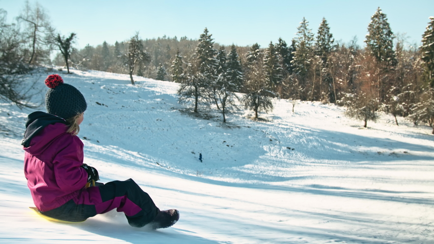 Tracking shot of a father and daughter having fun on the snow, enjoying the pleasures of sledding using plastic shovel sled. Royalty-Free Stock Footage #1081641011