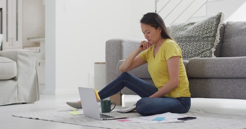 Focused asian woman sitting on floor and working remotely from home with smartphone and laptop. home office and freelancing concept.