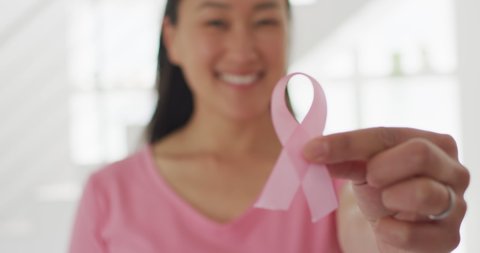 Happy asian woman in pink tshirt showing pink ribbon at home. health, prevention and breast cancer awareness.