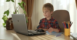 Child Study Online Lesson Video Conference Chat Using Laptop Computer. Kid Distance Learning at Home. Preschooler Boy Sits at Desk Table in Room Near Window 4K