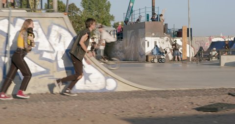 September 06 2021, St. Petersburg, Russia: Teenagers with dachshund in arms run away from someone or hurry somewhere, running past extreme park with ramps where youth ride bmx bikes and skateboards.