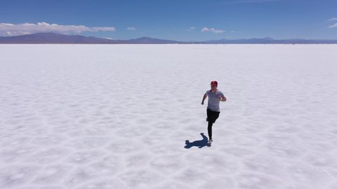 Young man running in the middle of the great salt flats of Jujuy in Argentina. Aerial drone 4K video. Sport and travel concept.