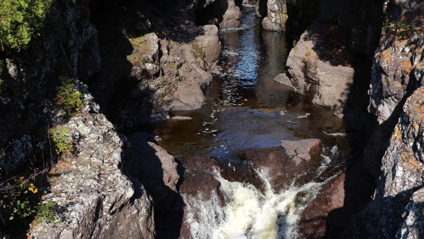 Water falls between rocks on the Temperance River at north shore of Lake Superior in northern Minnesota. Slow motion nature clip of cascade under pedestrian bridge with tilt up to highway bridge.