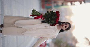 Happy woman carries and sniffs bouquet of flowers walking around the city, vertical video