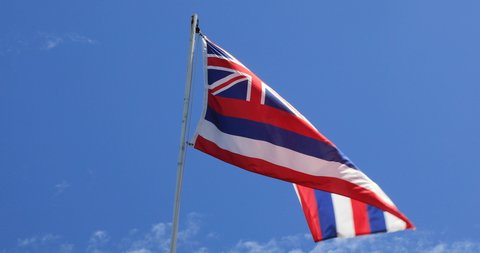 Stationary handheld footage of Hawain flag blowing in the wind with blue sky background, Hawaii, USA