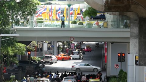 BANGKOK, THAILAND - 11 JULY, 2019: Intersection on busy city street. People on motorcycles and cars riding on crossroad under pedestrian bridge on busy street