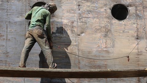 DHAKA, BANGLADESH - OCTOBER 30, 2021: The shipwreck ship break and demolition business with metal vessels and boats on the shore where manual labor is welding and sandblasting the metal sheets