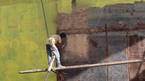 DHAKA, BANGLADESH - OCTOBER 30, 2021: The shipwreck ship break and demolition business with metal vessels and boats on the shore where manual labor is welding and sandblasting the metal sheets