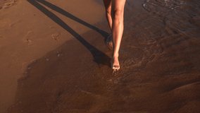 Handheld 4k video footage of two beautiful young adult tanned female barefoot legs walking on wet sand of sea beach of tropical summer resort