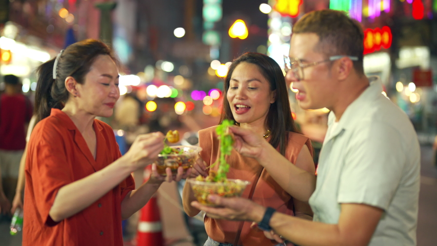 4K Group of Asian woman and LGBTQ people friends tourist enjoy eating traditional street food bbq seafood grilled squid with spicy sauce together at china town street night market in Bangkok, Thailand Royalty-Free Stock Footage #1081666886