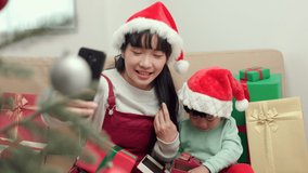 Cute Asian Mother and son using smartphone video call to family giving the present gift box each other playing peekaboo into camera. In happy moment the christmas eve festival at home.