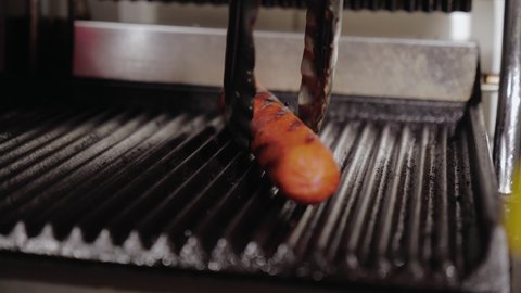 street food at a kiosk in a big city. the chef removes the sausage from the grill and puts it in the hot dog