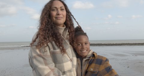Portrait of mother and son embracing on beach holiday in autumn