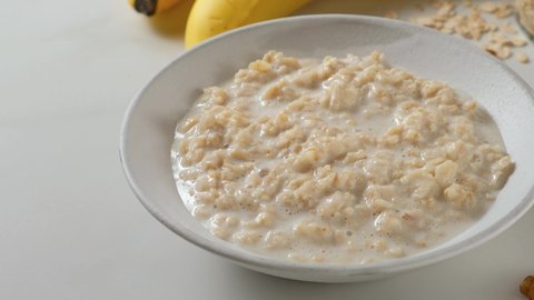 Healthy breakfast. Hand puts banana in oatmeal porridge in a plate. 4k video. Tasty diet food