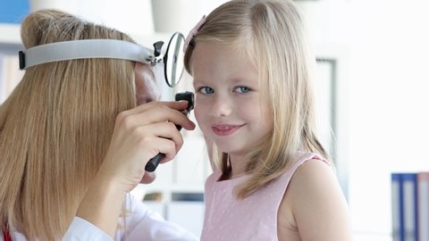 Ent with frontal reflector examining little girl ear with otoscope 4k movie