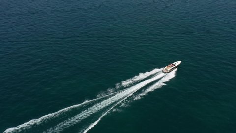 White boat movement on the water top view. Luxurious big boat fast diagonal movement on blue water, aerial view. Expensive, luxury, high-speed boat moving on the water top view.