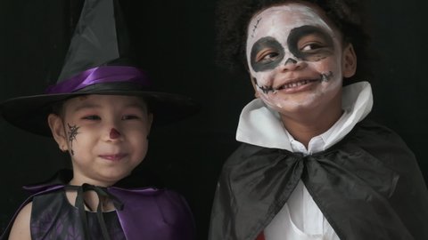 Girl and boy in witch and dracula costumes are pretending to be haunted at the halloween party.black background.