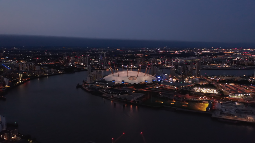 Evening aerial view of Millennium Dome. O2 arena at night. Illuminated city streets and buildings. London, UK