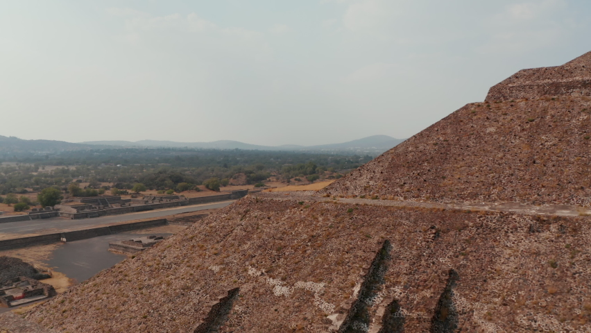 Forwards fly around corner of pyramid. Revealing panoramic view of dry landscape and ancient site.Ancient site with architecturally significant Mesoamerican pyramids, Teotihuacan, Mexico