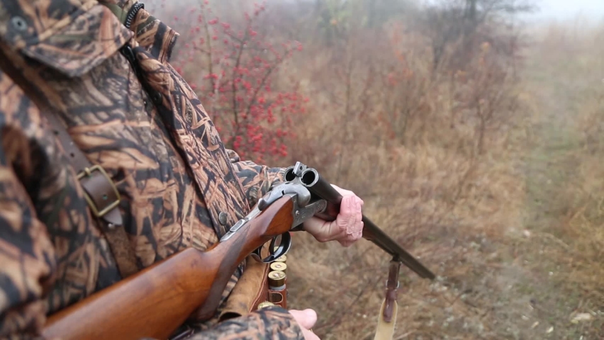 hunter man with gray beard in hunter suit load cartridges in a double-barreled rifle and makes aiming wiring