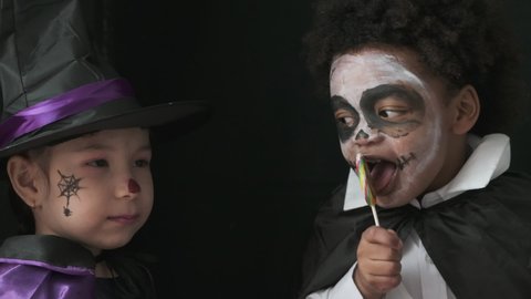 Girl and boy in witch and dracula costumes are pretending to be haunted at the halloween party with black background.