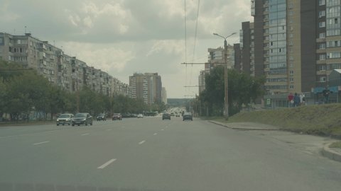 Moving footage of a car driving on the road on one of the streets of Chelyabinsk, Russia. The movement of the car against the background of tall houses in summer. The driver is driving straight.