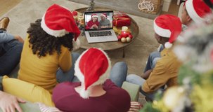 Diverse family with santa hats using laptop for christmas video call with smiling couple on screen. christmas, festivity and communication technology.