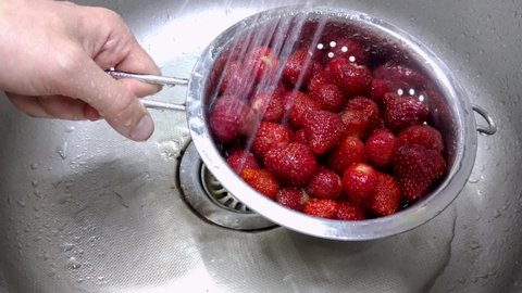 male hand holds a colander with strawberries underwater. many thin jets of water pour on the berries from above, washing the strawberries from dirt